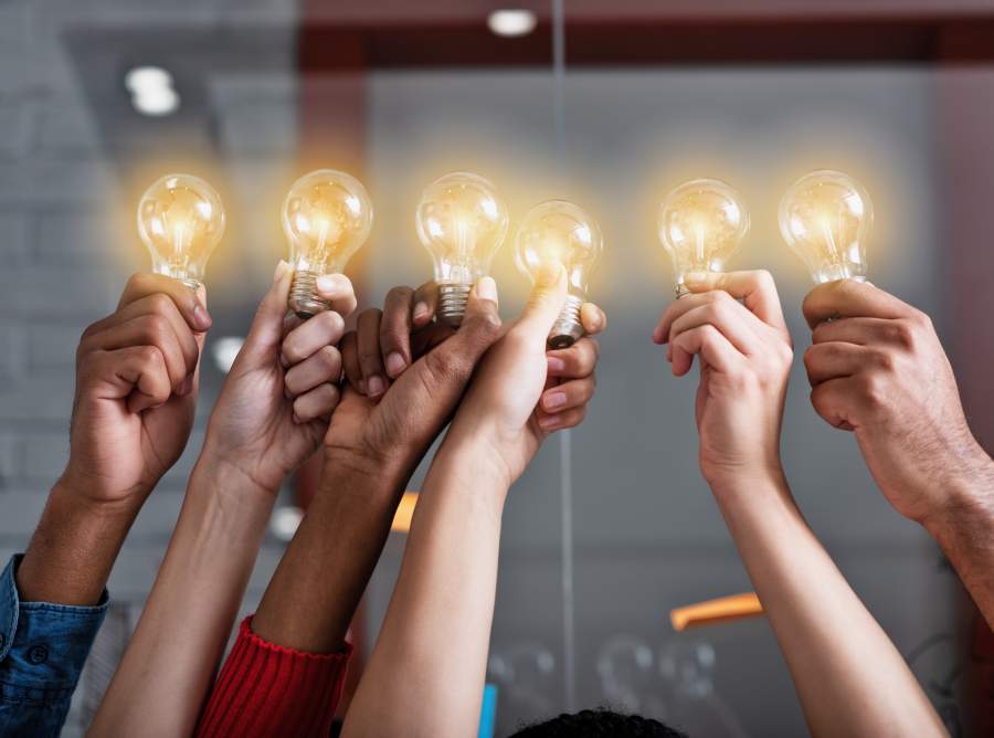 Mehrere Hände halten leuchtende Glühbirnen zusammen