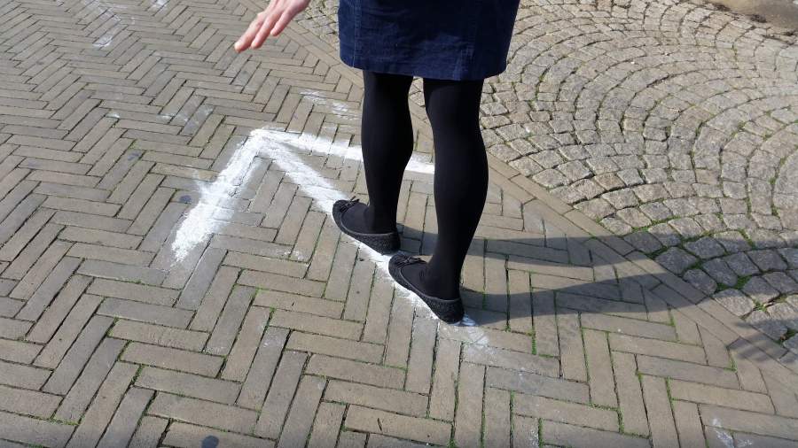 Eine Frau balanciert auf einem Pfeil aus Kreide auf dem Boden